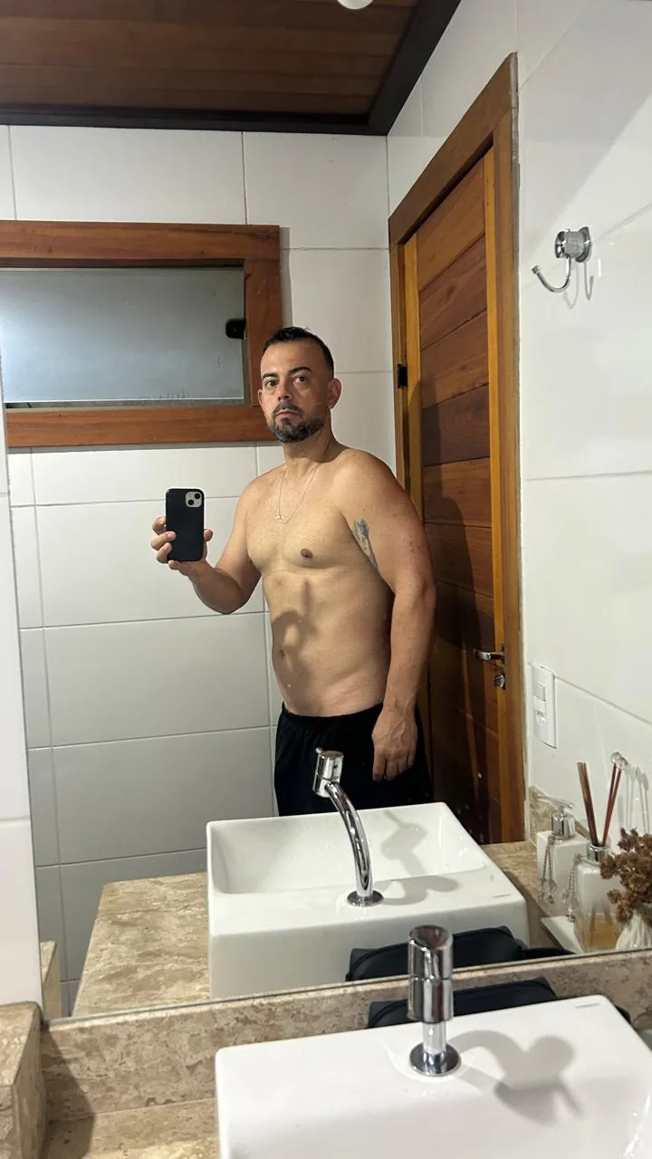 Henrique hoje, sem camisa, em frente ao espelho do banheiro, já treinando com o Igor, com o abdômen mais definido