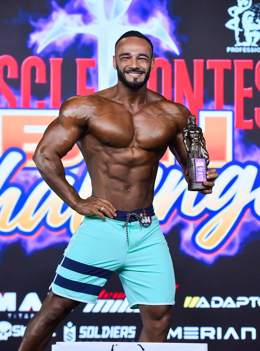Igor Silva no palco de uma competição de fisiculturismo, segurando o troféu